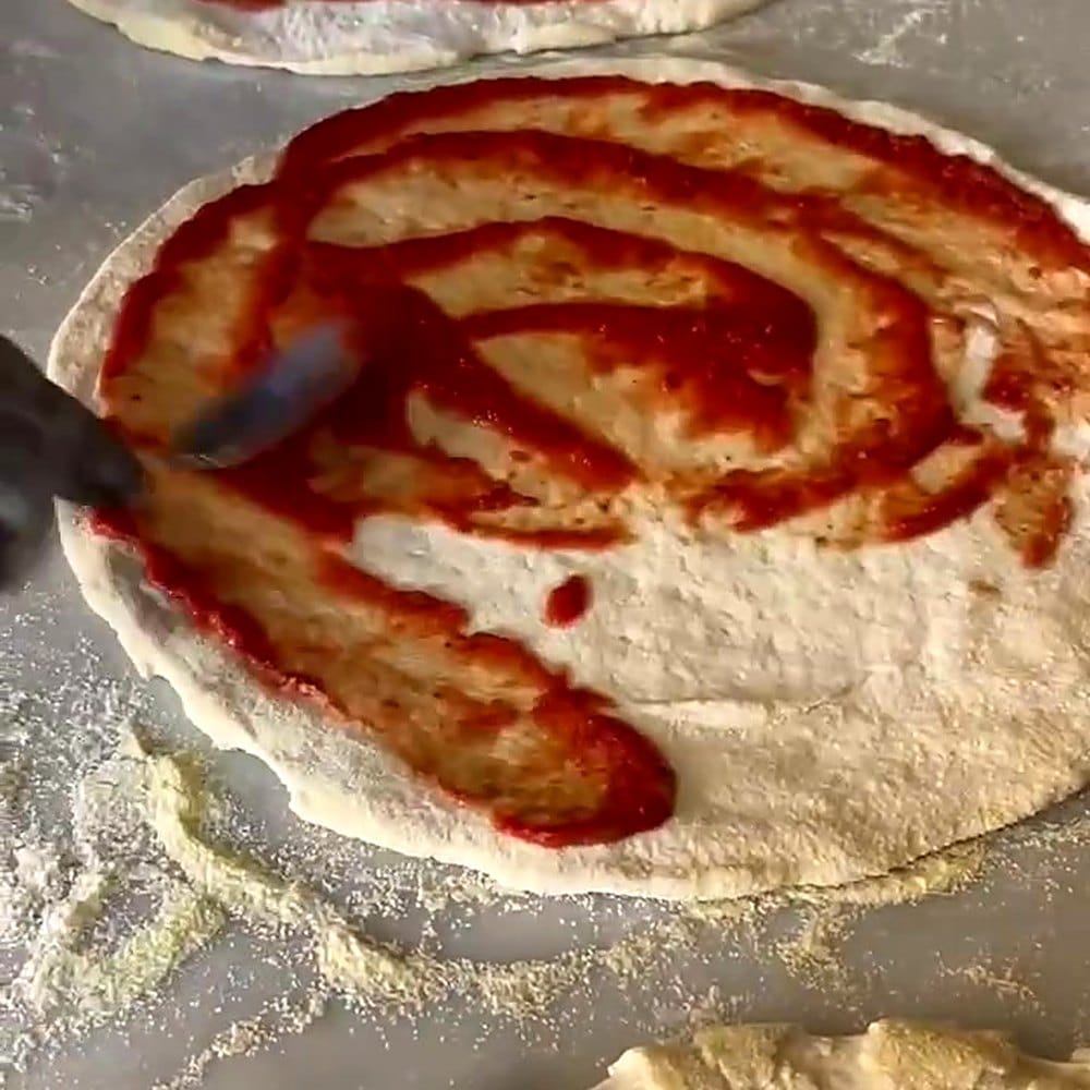 Sauce tomate etalee en spirale a la louche sur une pizza de 33 cm